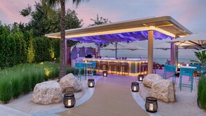 Un bar en la playa con terraza de madera, asientos y vista al océano.