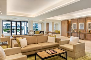 A modern hotel lobby with a beige sofa set, a chessboard on a coffee table, and a view of the outdoor area. - Intercontinental Fujairah Resort (FUJAIRAH)
