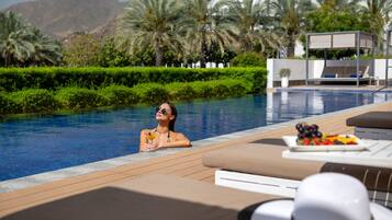A poolside area with lounge chairs, a table with fruit, and a view of a mountain.
