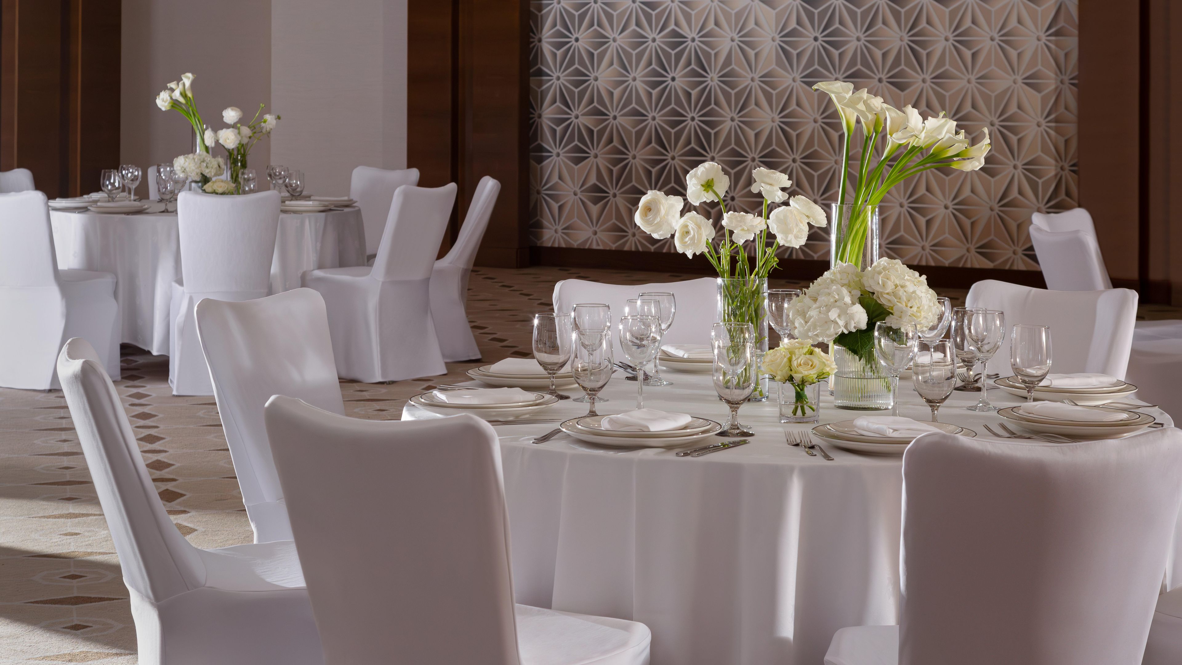 A banquet hall with round tables set for dining, white chairs, and floral centerpieces.