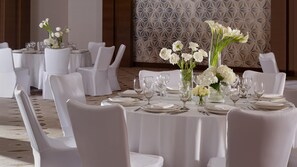 A banquet hall with round tables set for dining, white chairs, and floral centerpieces.