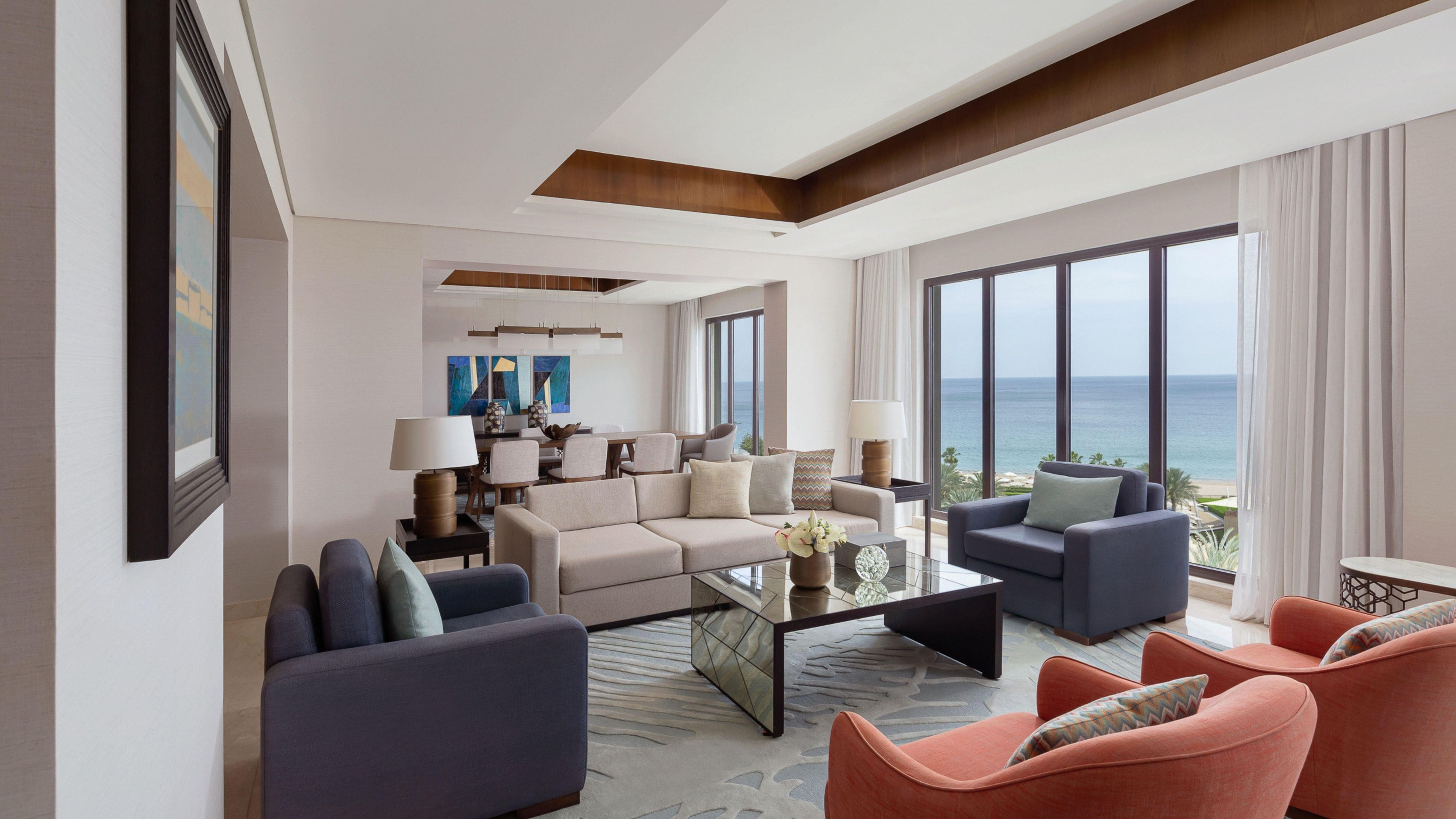 A modern hotel room with a living area, dining space, and a large window with a view of the ocean.