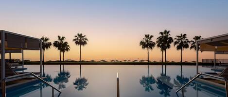 A pool with clear water reflecting palm trees and a sunset in the background.