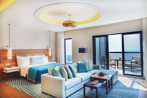 A hotel room with a bed, a sofa, a coffee table, a nightstand, a lamp, and a view of the sea through a balcony door. - Intercontinental Fujairah Resort (FUJAIRAH)