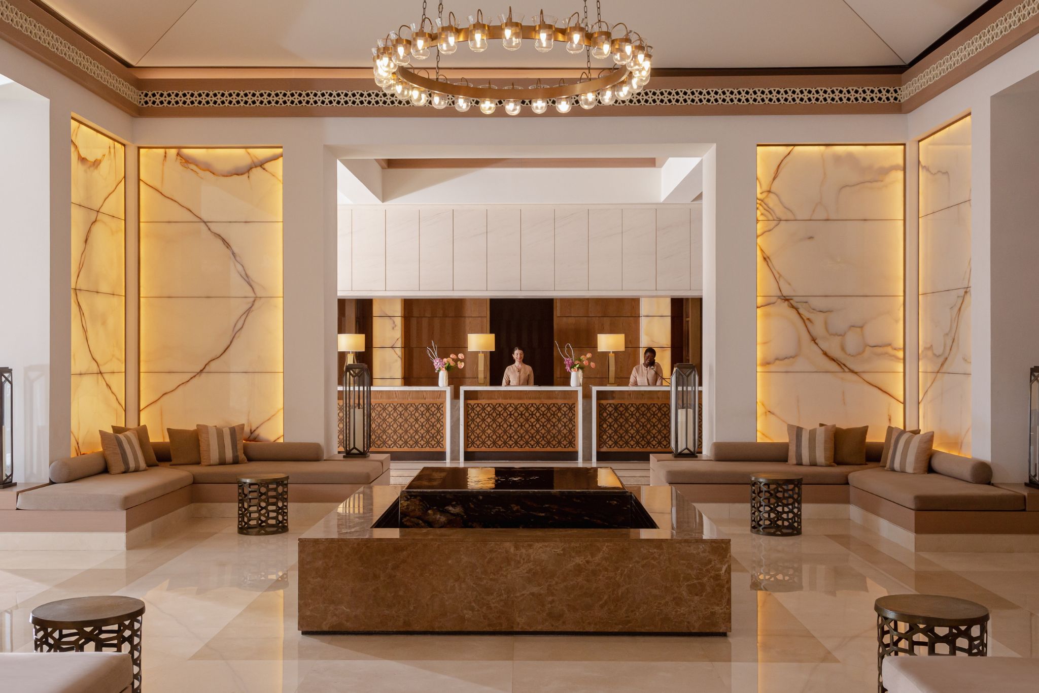 A lobby with a reception desk, sofas, a chandelier, and marble walls.