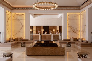 A lobby with a reception desk, sofas, a chandelier, and marble walls. - Intercontinental Fujairah Resort (FUJAIRAH)