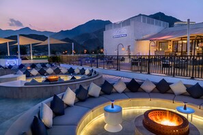 A modern outdoor seating area with a fire pit, cushioned seating, and a mountain backdrop. - Intercontinental Fujairah Resort (FUJAIRAH)