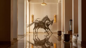 A hallway with a reflective floor, a geometric light fixture, and a wall-mounted sculpture of two horses.