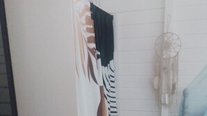 Ein Zimmer mit einem Bett, einem Nachttisch, einer Lampe, einem Traumfänger und einem Vorhang mit Blätermotiv.