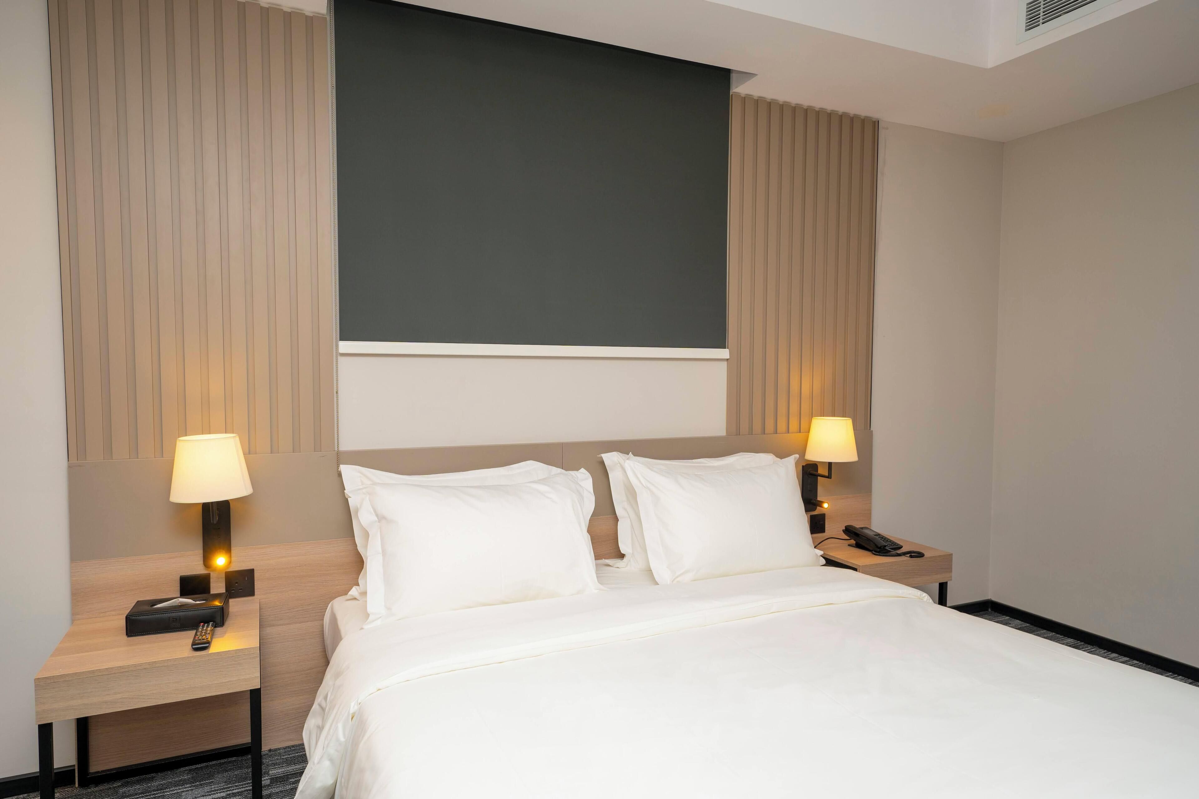 A hotel room with a bed, two bedside tables with lamps, a phone, and a large dark wall above the bed.