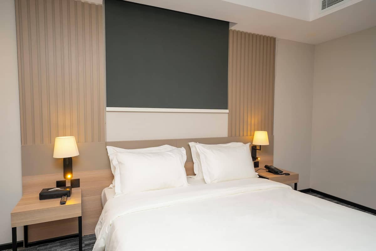 Une chambre d’hôtel avec un lit, deux tables de chevet avec des lampes, un téléphone et un grand mur sombre au-dessus du lit.