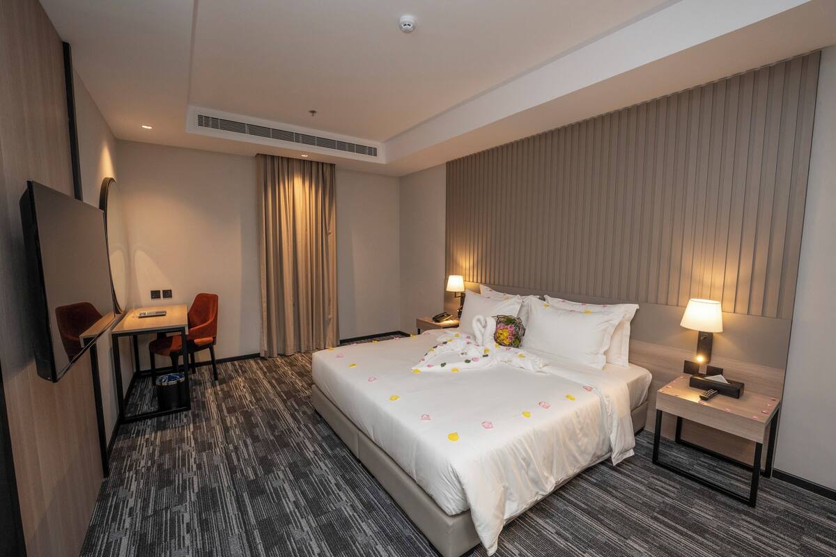 Une chambre d’hôtel avec un grand lit, un bureau avec une chaise, une télévision et une table de chevet avec une lampe.
