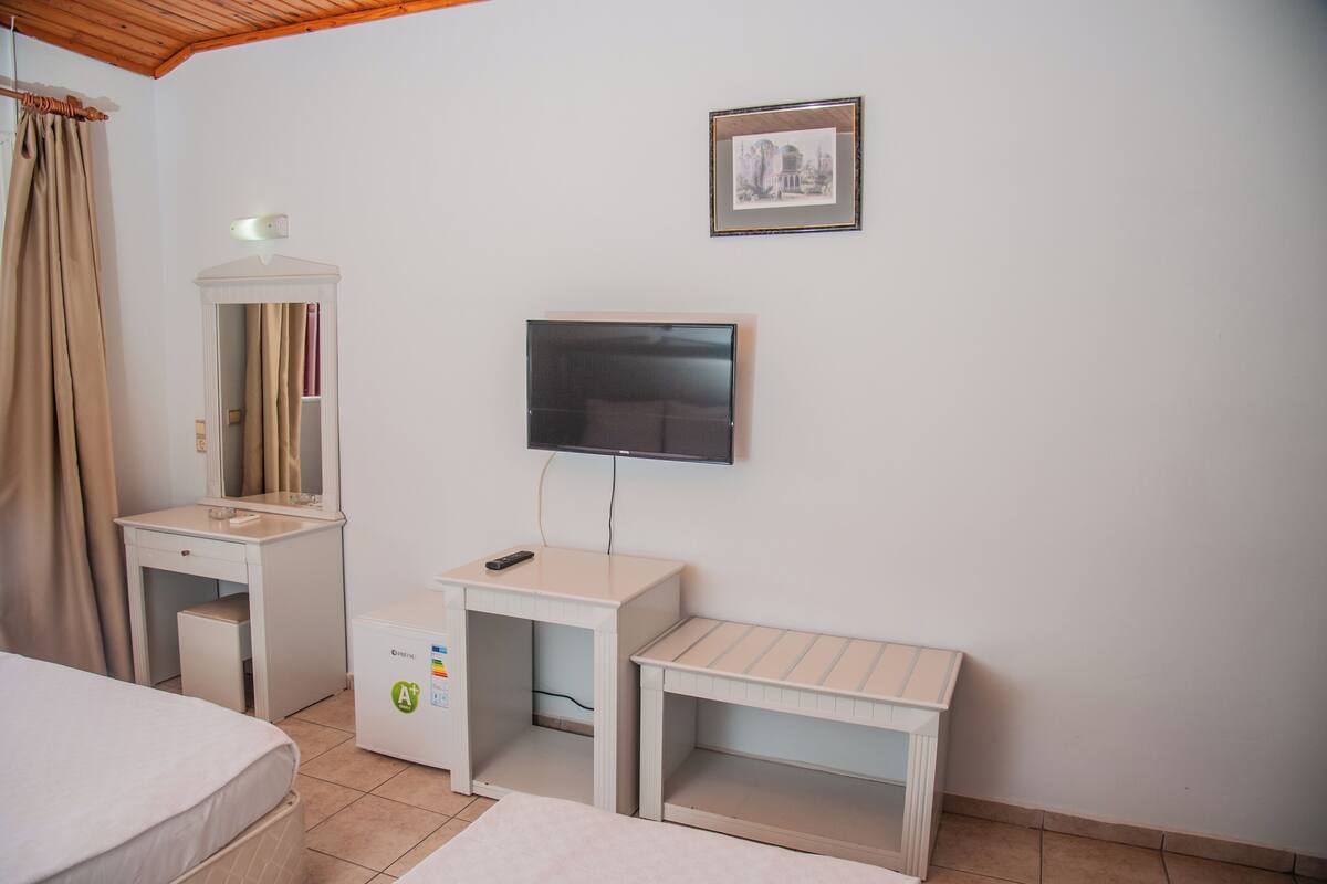 Una habitación de hotel con una cama, un escritorio con espejo, televisión y una mesita.