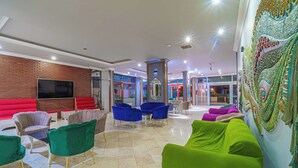 Un vestíbulo amplio con televisor de pantalla plana, asientos rojos y verdes, y un mural decorativo.
