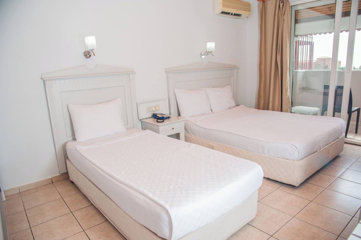 Una habitación de hotel con dos camas, una mesita de noche, un ventanal y una cortina.