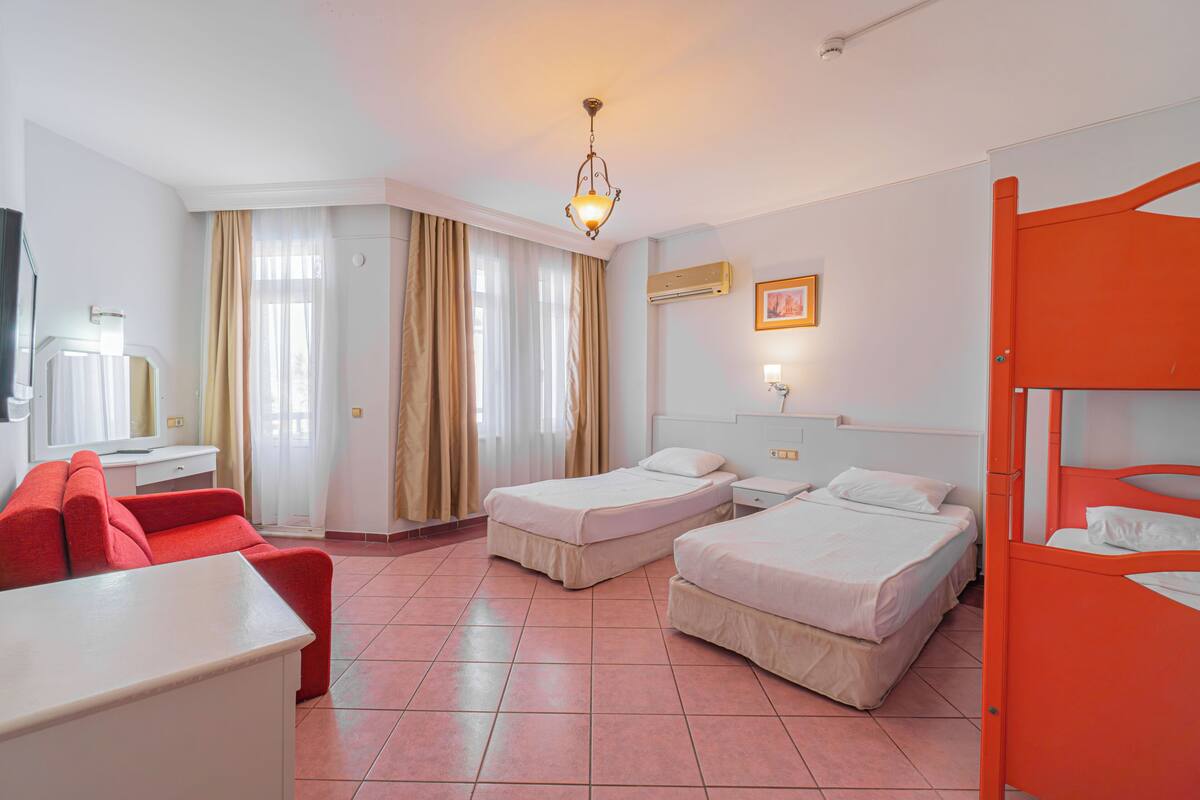 Una habitación de hotel con dos camas, un sofá rojo, un escritorio y una ventana con cortinas.