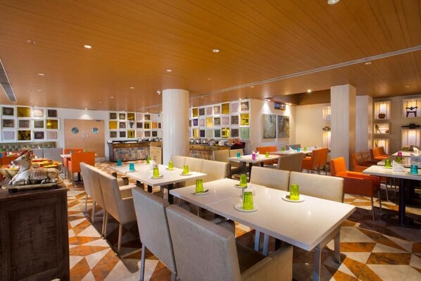 Un restaurant doté de plusieurs tables et chaises, d’un bar et d’un mur orné de tableaux.