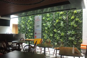 An indoor seating area with tables and chairs, a vertical garden wall, and a sign with logos. - Fountain Tree by TGI - JP Nagar, Bangalore (Bengaluru)