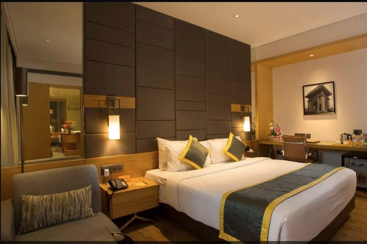 A hotel room with a bed, bedside table, chair, desk, and a mirror.