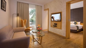 Una habitación de hotel con sofá, una mesa de vidrio con flores, televisor y cama con cabecera.