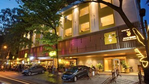 Un hotel con fachada moderna, mesas al aire libre y una entrada visible.