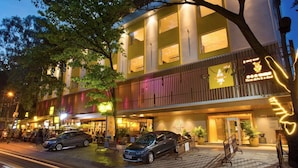 Un hotel con fachada moderna, mesas al aire libre y una entrada visible.