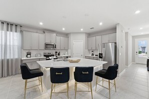 A modern kitchen with a central island, stainless steel appliances, and bar stools. - Themed 7BR Pool Home Solara, Flowrider Resort (Kissimmee)