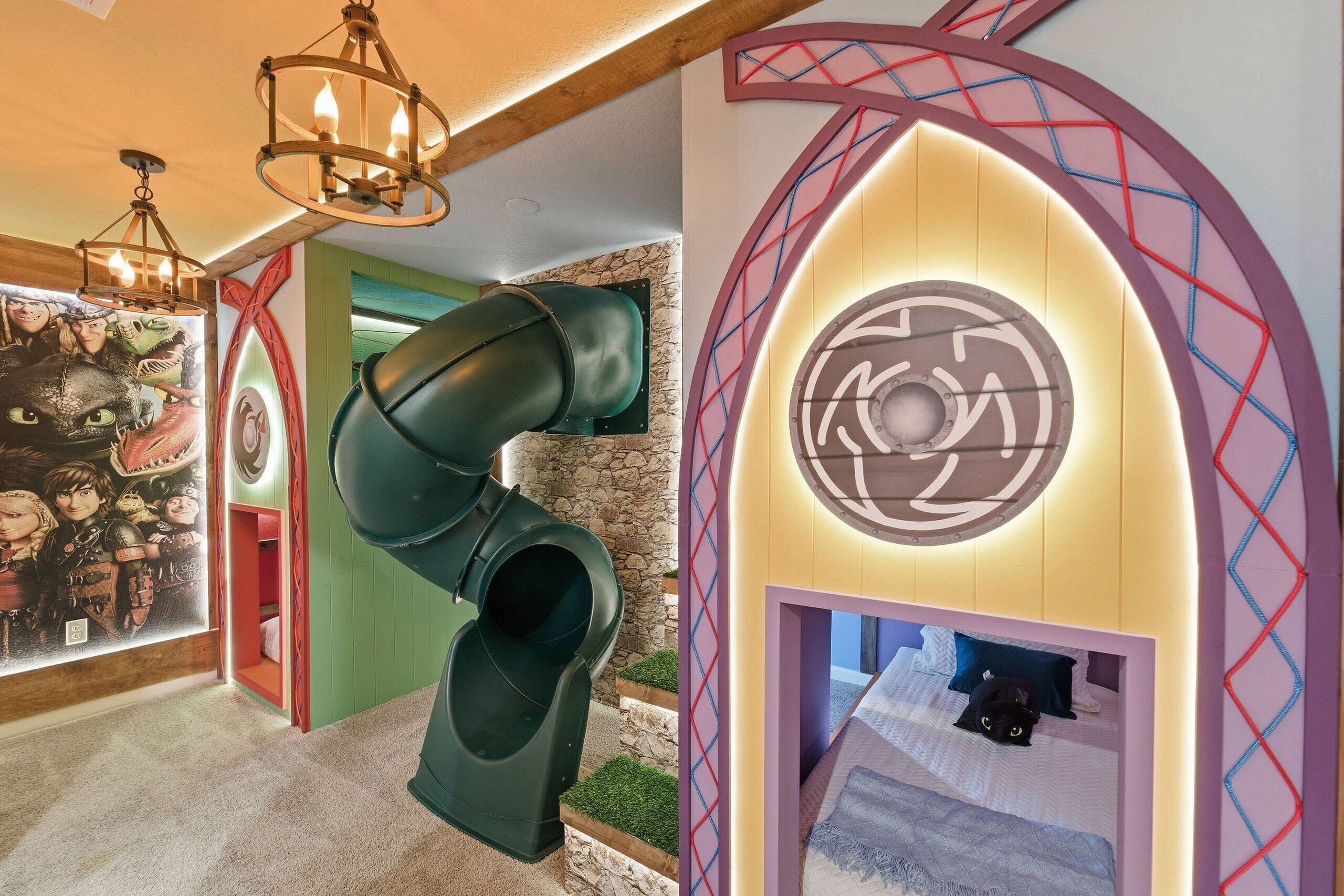 Un espace de jeux pour enfants avec un toboggan, une fresque murale et une salle à thème comprenant un lit et un chat.
