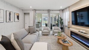 A modern living room with a sofa, armchairs, a coffee table, and a TV. - Themed 7BR Pool Home Solara, Flowrider Resort (Kissimmee)