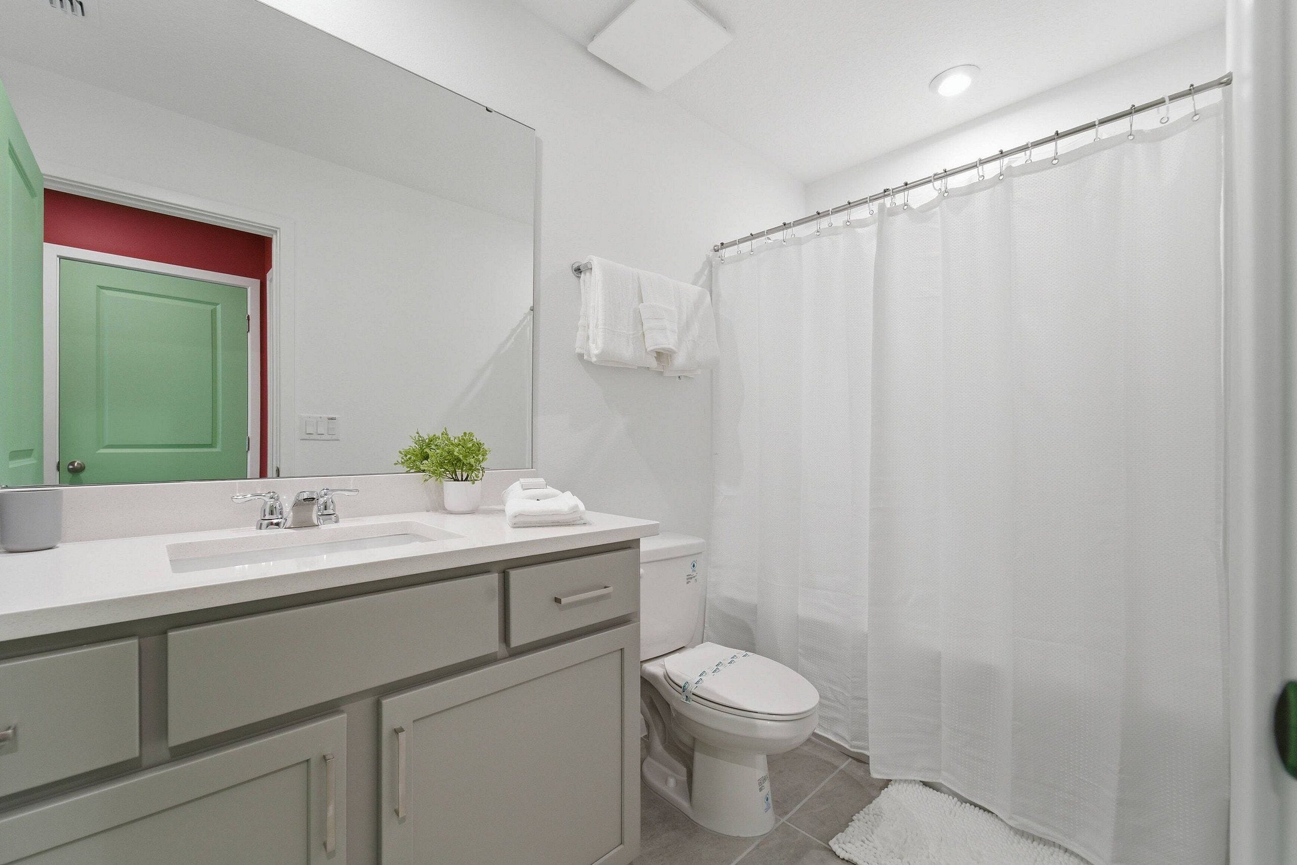 Un baño con un lavamanos blanco, una puerta verde, un inodoro blanco y una cortina de ducha.
