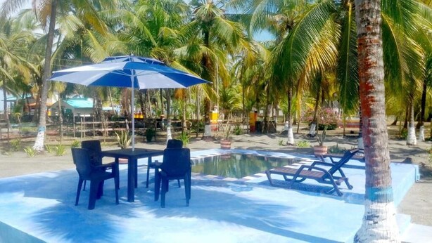 A pool area with lounge chairs, a table with chairs, and an umbrella. - Cabaña Olas Del Mar (San Bernardo del Viento)