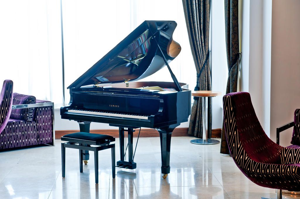 A grand piano in a well-lit room with a modern chair and a small table.