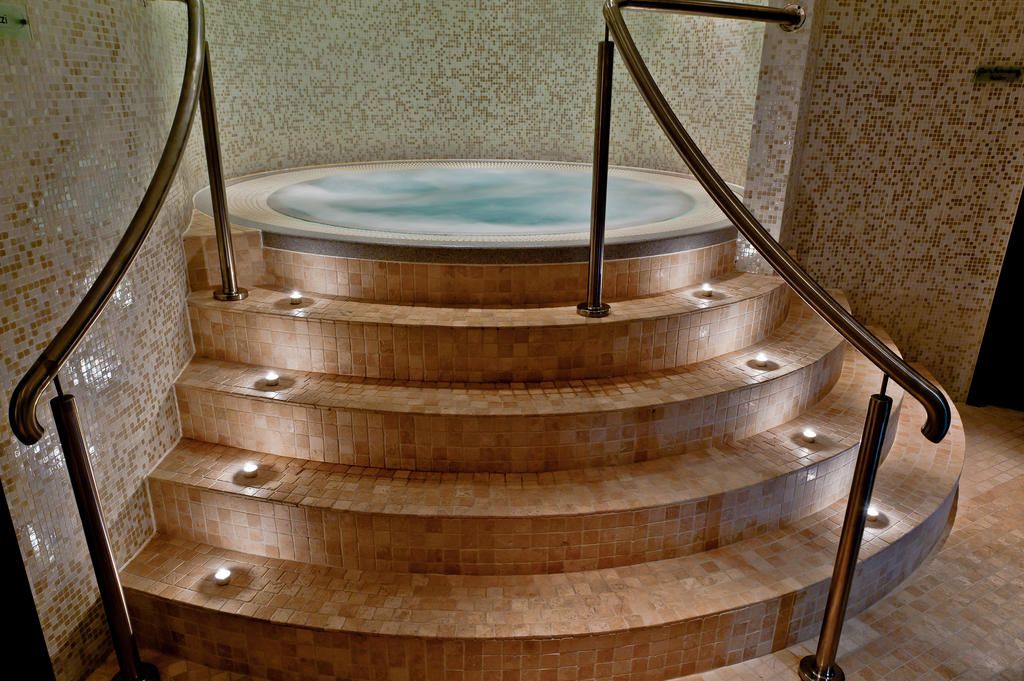 A set of curved stairs leading to a hot tub area with a tiled floor and metal railings.