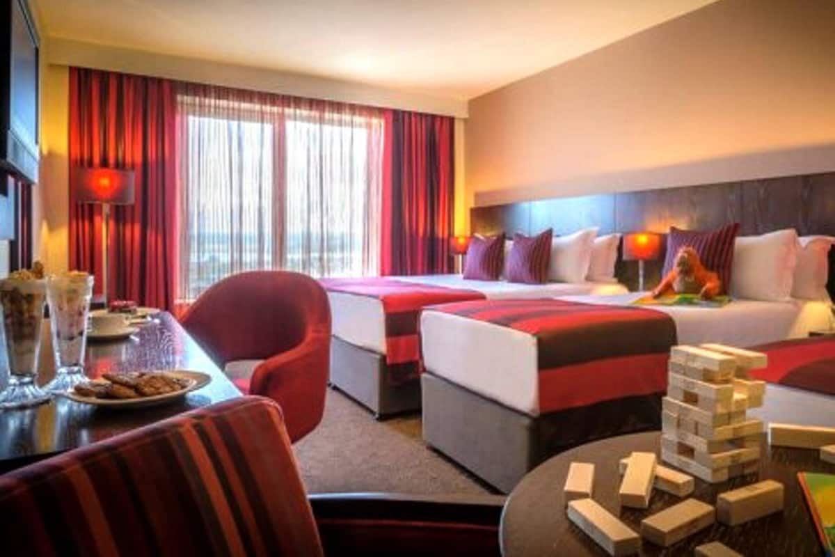 Una habitación de hotel con dos camas, una mesa de comedor y un plato de comida, además de un rompecabezas sobre la mesa.