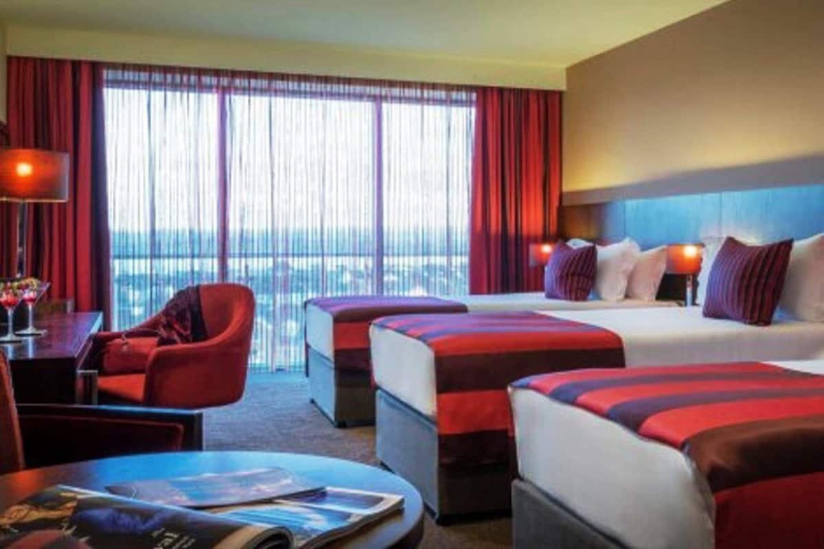 Una habitación de hotel con dos camas, un escritorio, una silla y un ventanal con cortinas.