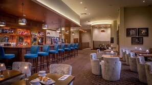 A bar area with multiple seating options, including bar stools and cushioned chairs, and a reception desk in the background. - Loughrea Hotel & Spa (Loughrea)