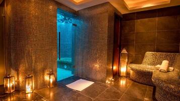 A spa room with mosaic walls, a seating area, and a visible shower.