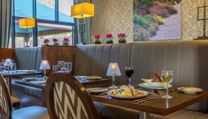 A restaurant with booths, tables, and a view of a garden.
