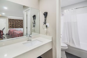 Ein Badezimmer mit weißem Waschbecken, einem Spiegel, einem an der Wand montierten Föhn, einer Toilette und einer Duschvorhang.