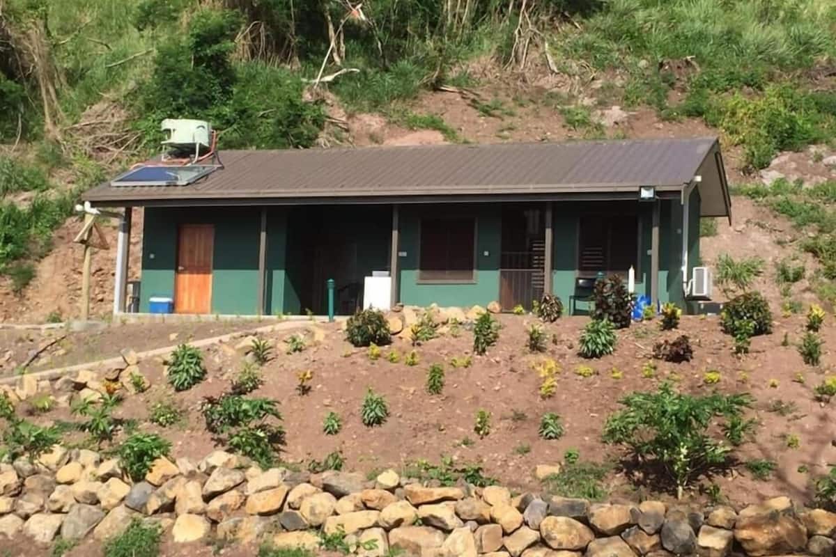 A single-story building with a flat roof, a front porch, and a small garden area with rocks and plants.