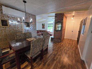 Ein Essbereich mit Holztisch und -stühlen, einer Ziegelwand als Akzent und ein Wohnzimmer mit Sofa und Gemälde.