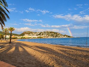 Ein Strand mit einem Berg im Hintergrund, einem klaren Himmel und einem Regenbogen.