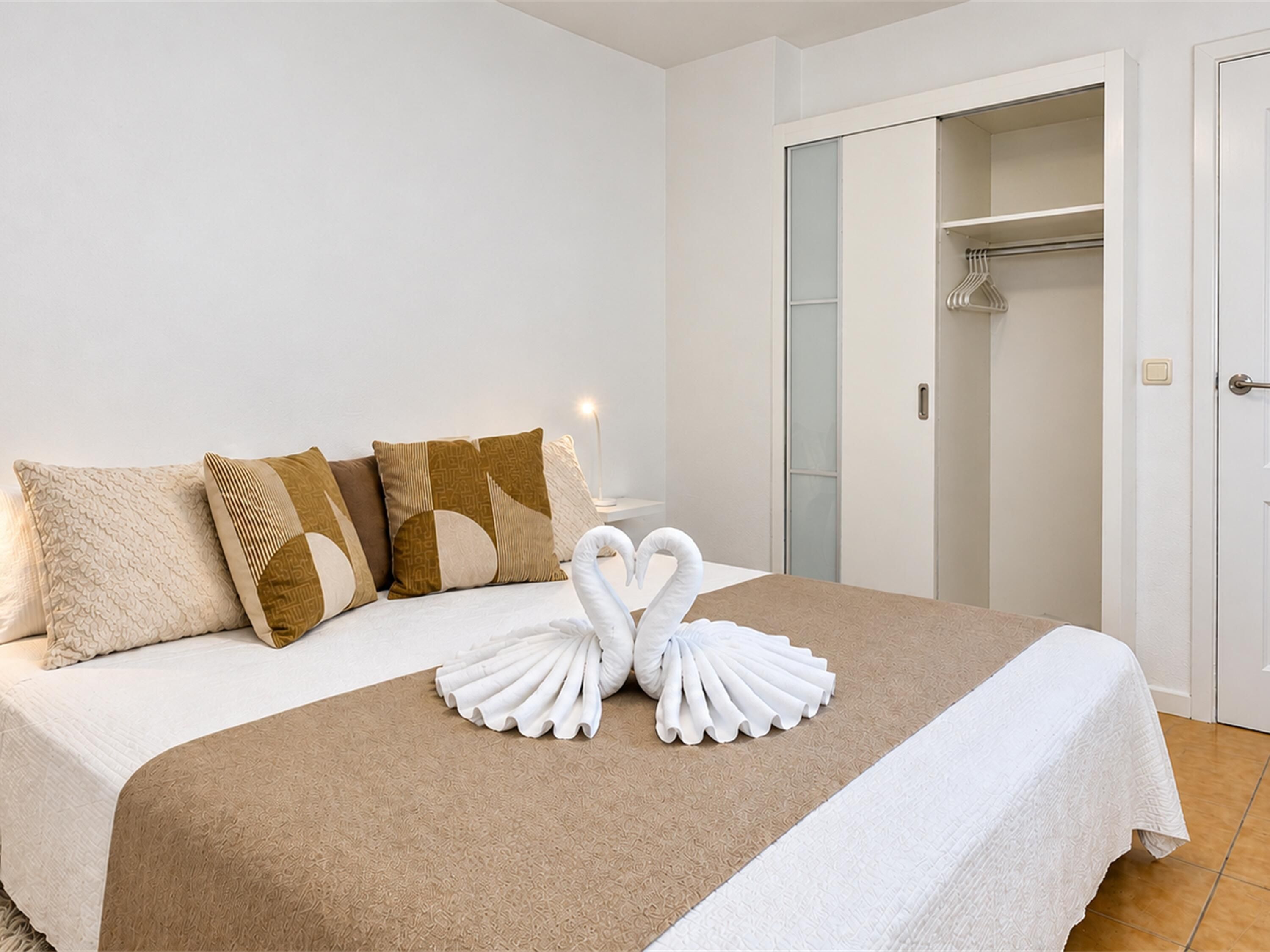 A hotel room with a bed, pillows, a swan-shaped towel arrangement, and a wardrobe.
