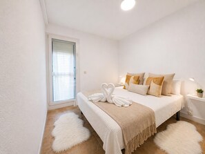 Ein Schlafzimmer mit Bett, Kissen, Nachttisch, Lampe, einer Zimmerpflanze und einem flauschigen Teppich.