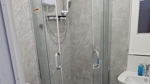 Moderni kylpyhuone, jossa on lasiseinällä varustettu suihku, valkoinen wc-istuin ja jalallinen pesuallas.