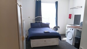 Une chambre avec un lit, un lave-linge et un petit bureau.