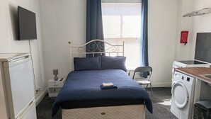 Une chambre avec un lit, un lave-linge, une télévision, une chaise et une petite table.