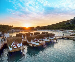Wasserbungalows mit Strohdächern, Holzterrassen und Liegestühlen.
