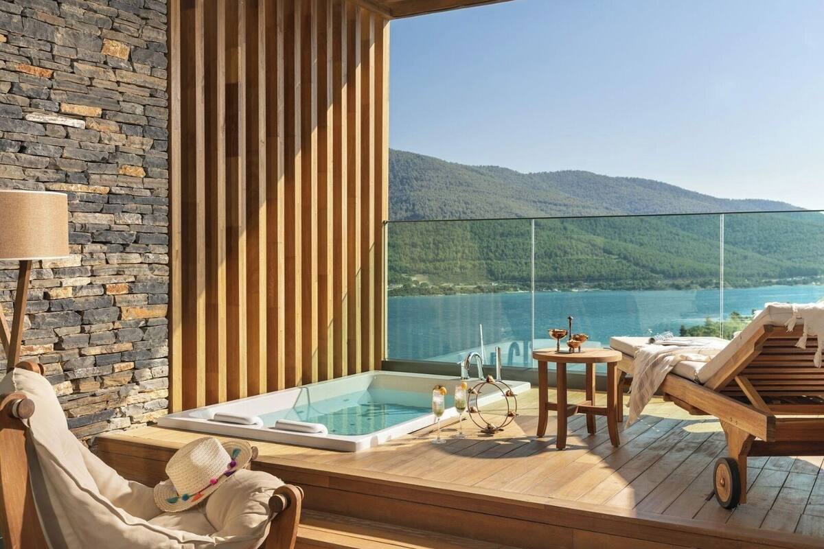 A balcony with a hot tub, wooden furniture, and a view of a lake and mountains.