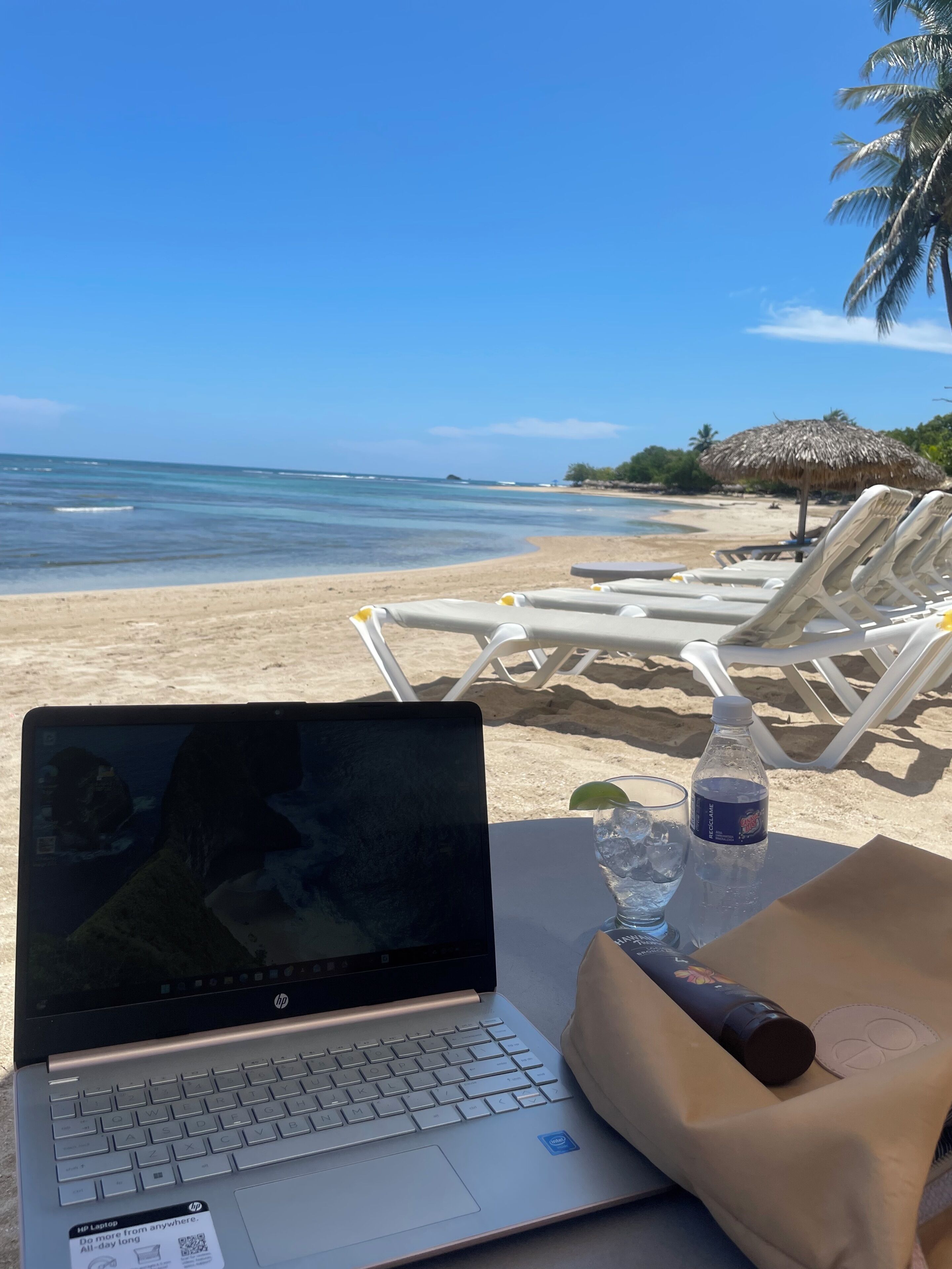 Vista con playa, una computadora portátil sobre una mesa, una botella de agua y un bolso.